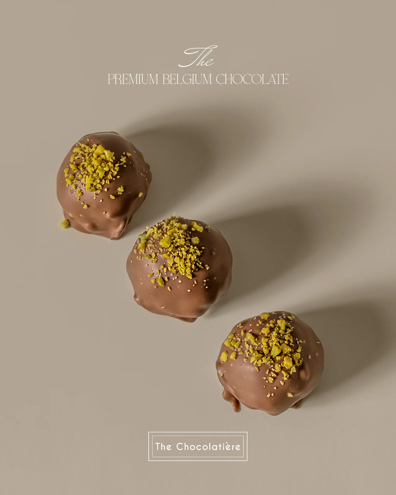Three pistachio-topped chocolates on a warm neutral surface.